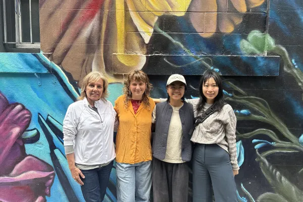 four SF Public Press workers stand in front of a colorful mural